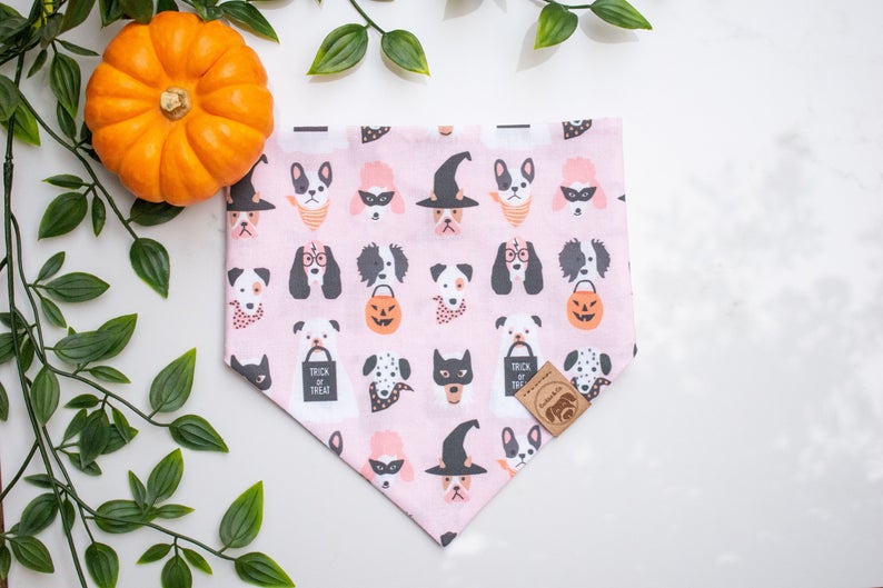 Howl-O-Ween bandana print, with different breeds of dog faces dressed in halloween fashion and bandanas on a light pink background