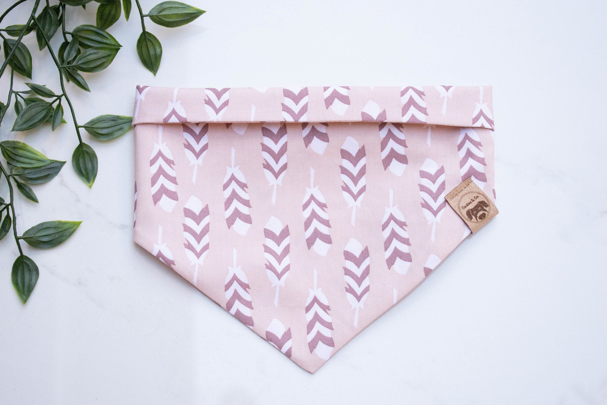 Feathers bandana print, featuring columns of white and brown feathers running different directions, on a light pink background