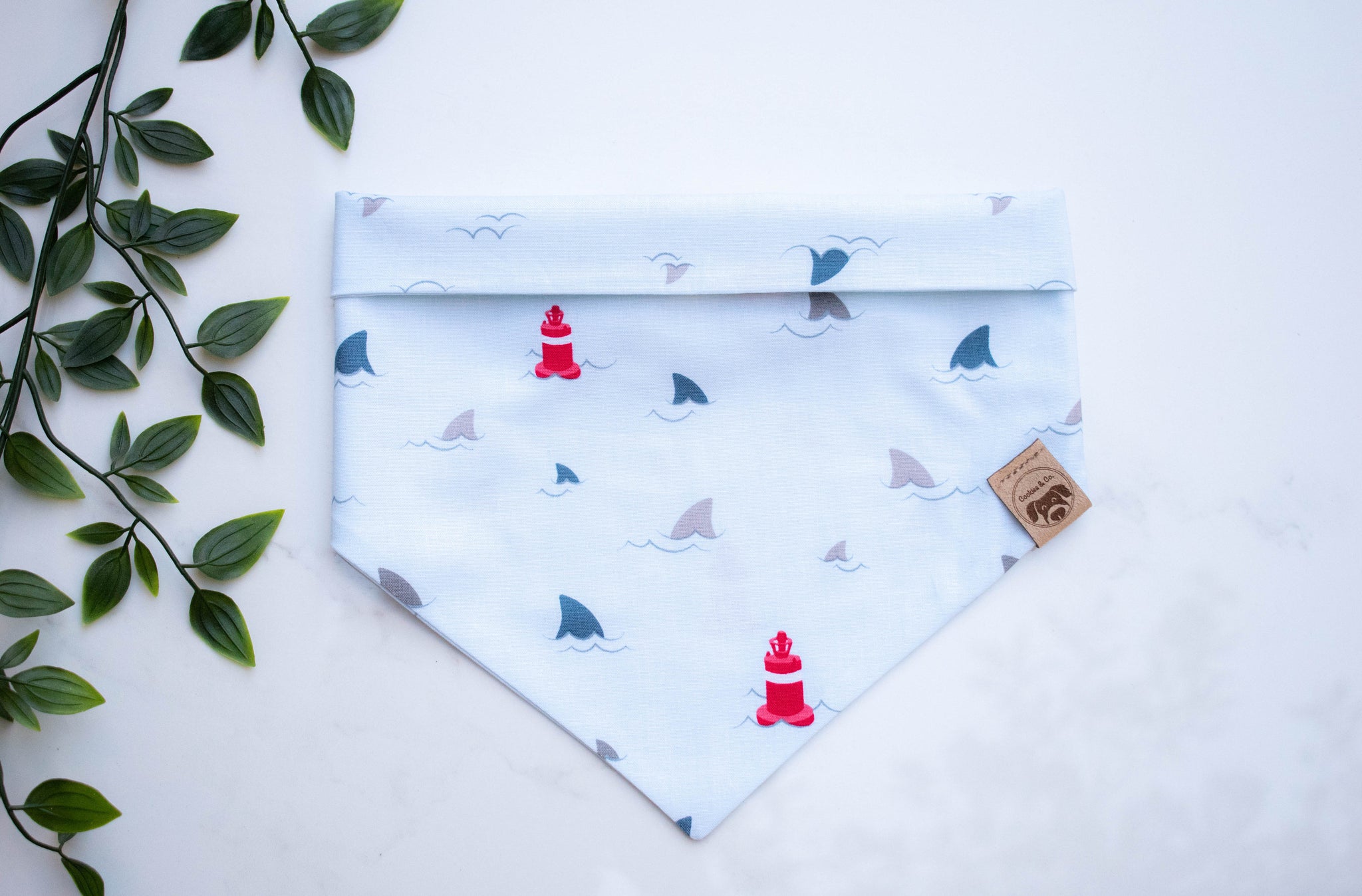 Shark Week bandana print, featuring multiple shark fins above water surface, with red floating buoys on a light blue fabric
