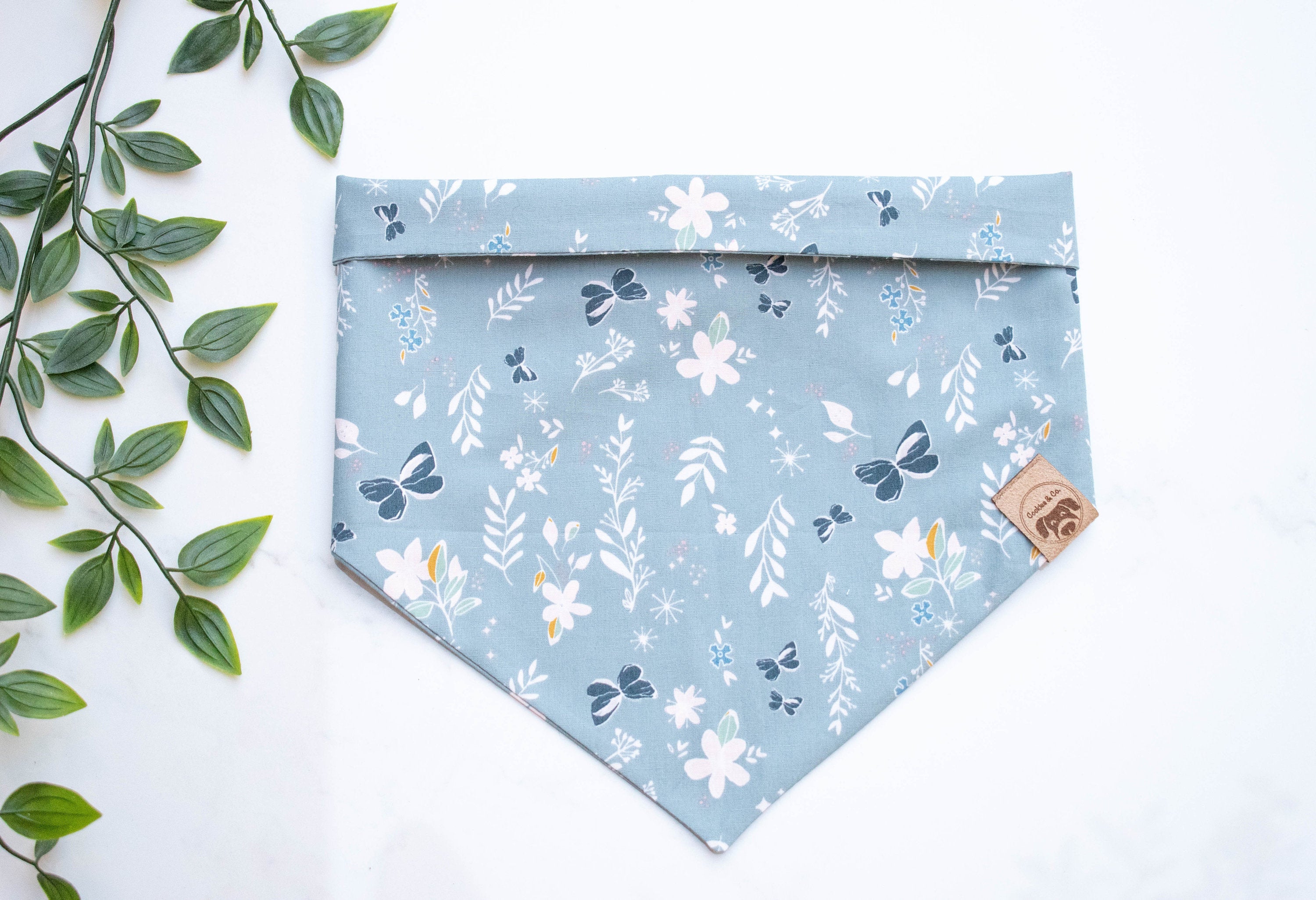 Flower Fields bandana print, featuring dark blue butterflies and white flowers and ferns on a light turquoise fabric