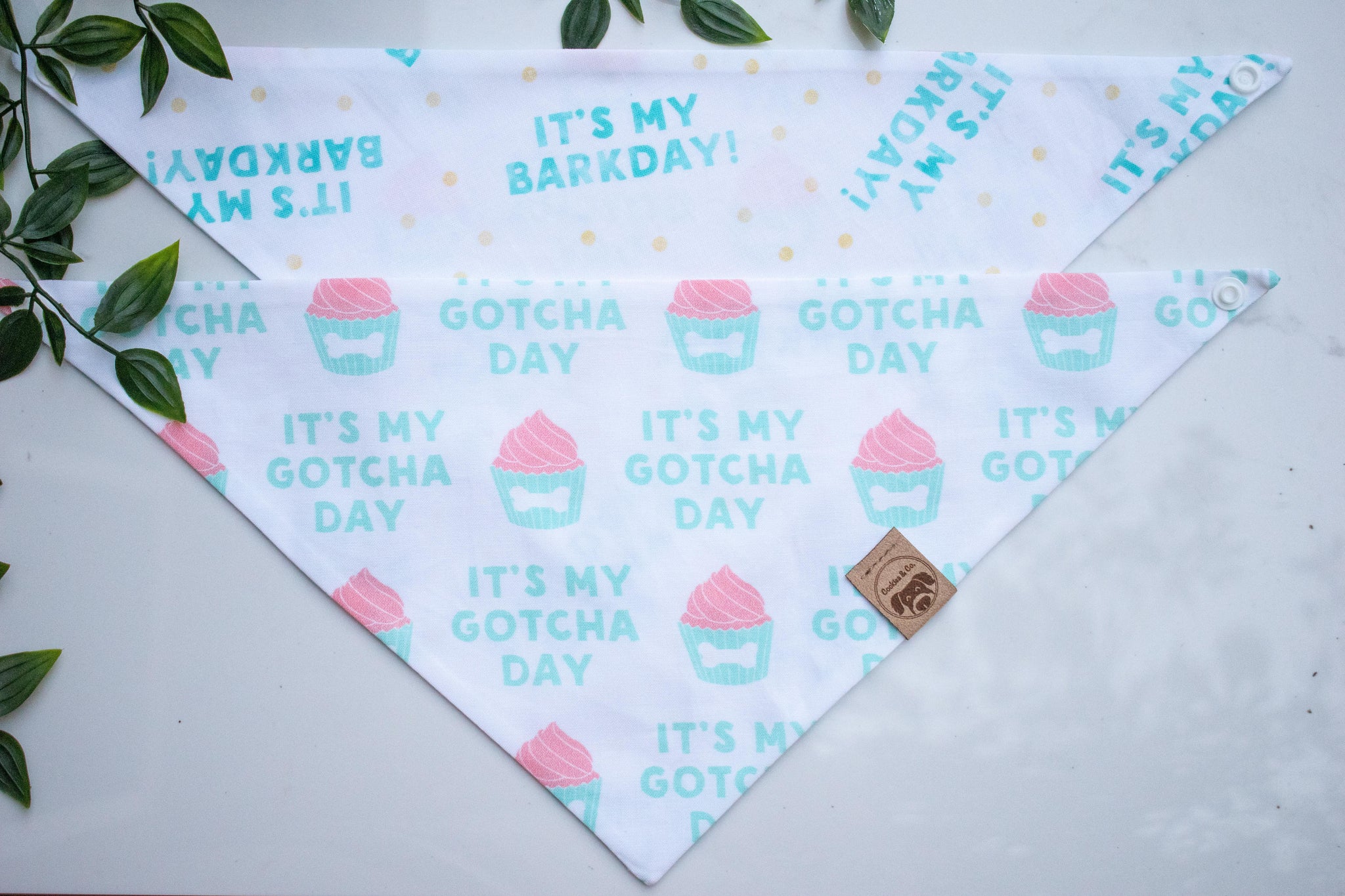 Reversible Gotcha and Barkday bandana print, with one side featuring a repeating pattern of 'Its My Gotcha Day' slogan and a pink cupcake in a light blue cupcake baking cup with a white bone icon on a white background, and the other side featuring a repeating pattern of 'Its My Barkday' slogan with yellow confetti on a white background.