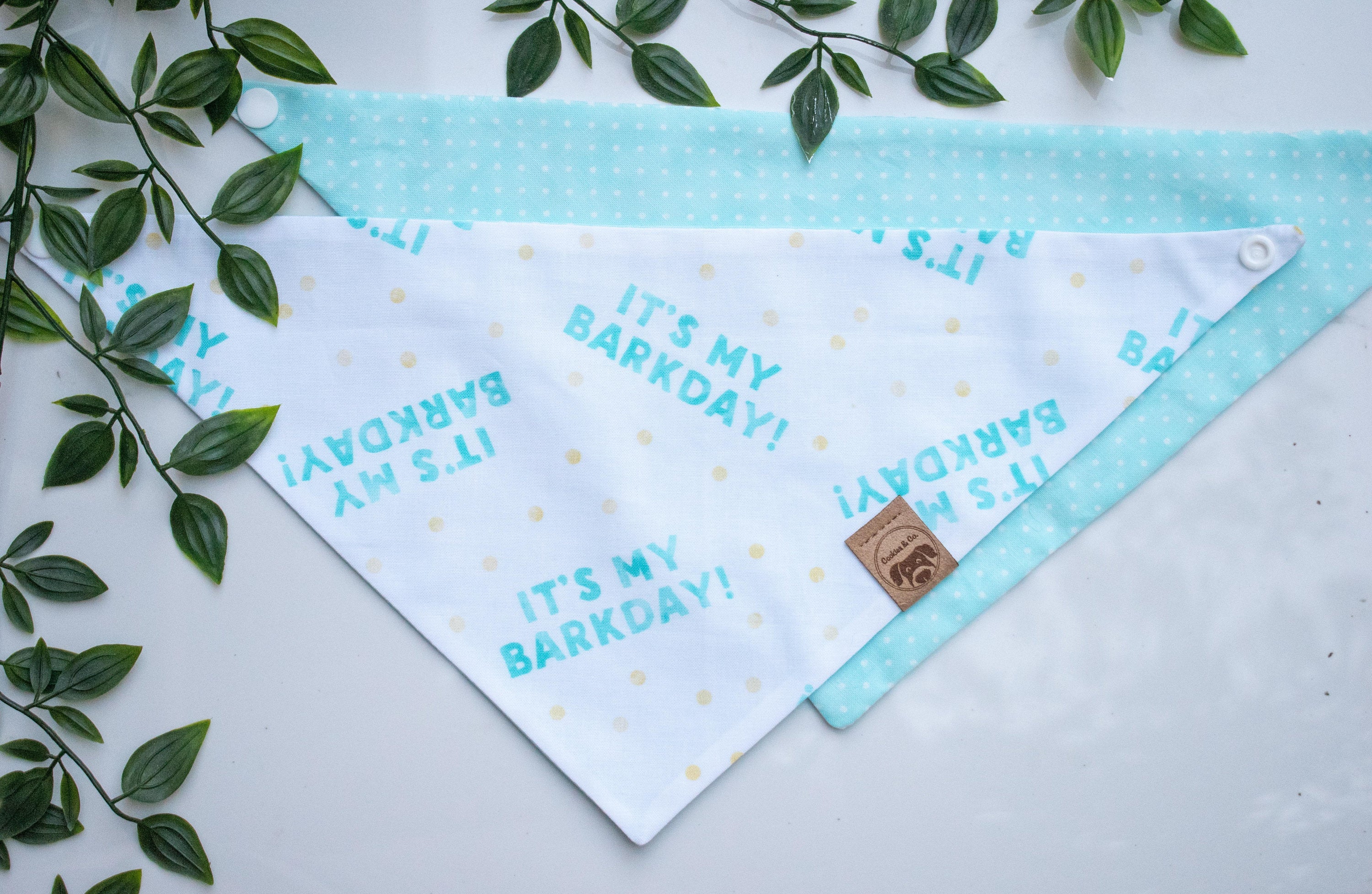 Reversible Gotcha and Dip N' Dots bandana print, with one side featuring a repeating pattern of 'Its My Gotcha Day' slogan and a pink cupcake in a light blue cupcake baking cup with a white bone icon on a white background, and the other side featuring white mini polka dot print on a light blue background